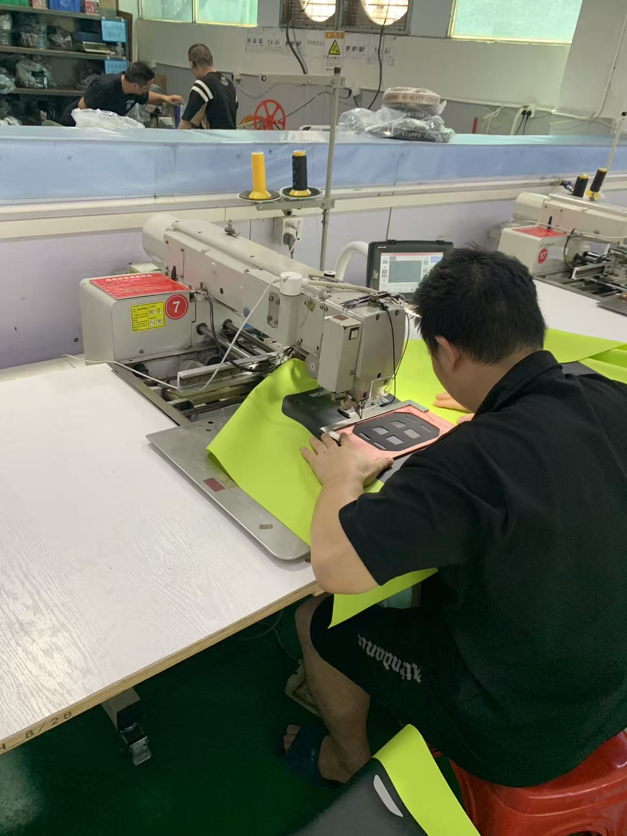 Programmable pattern sewing machine stitching a reinforcement panel onto fluorescent waterproof fabric
